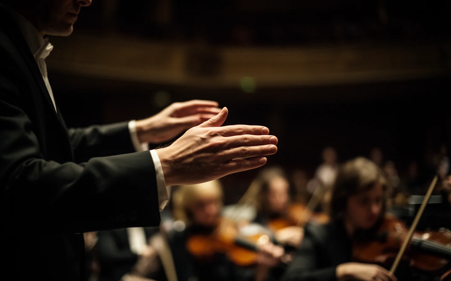 Conductor's hands mid-downbeat, orchestra blurred behind in warm light