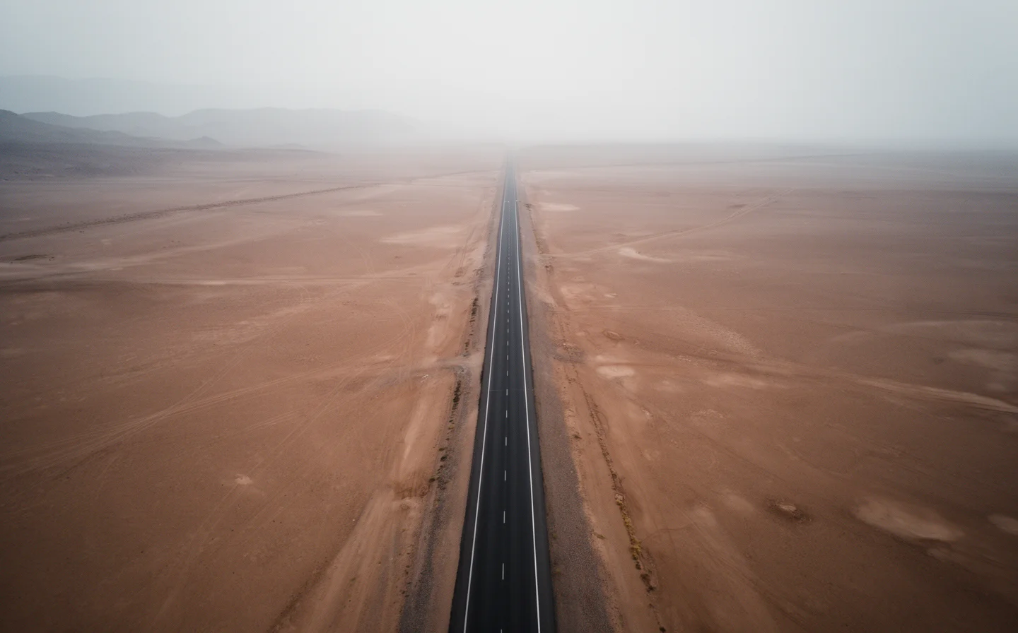 Single road cutting through empty desert landscape, aerial view